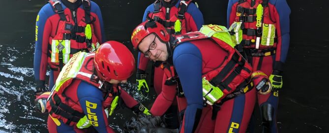 DLRG Rettungskräfte sind im Wasser. Sie halten in der Hand eine Skulptur