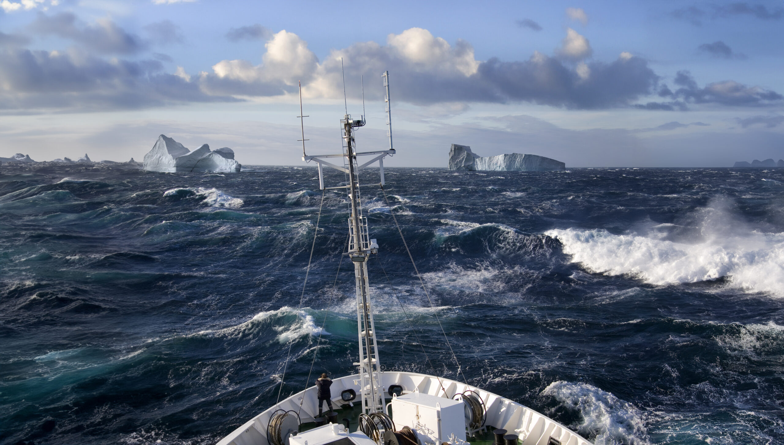 Das Foto zeigt das Bug eines Schiffes in der Arktis mit viel Eis und Wellen.