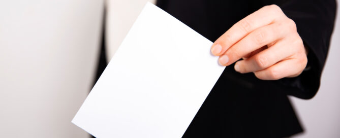 Das Foto zeigt die Hand einer Frau, die einen Wahlumschlag in eine Wahlurne einwirft.