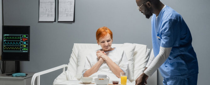 Ein Krankenpfleger bringt einer Patientin im Krankenhaus Frühstück ans Bett.