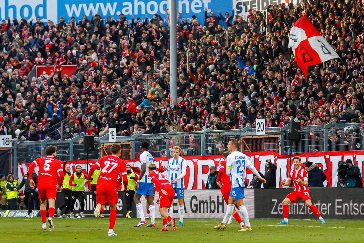 Spieler von Energie Cottbus vor der vollen Tribüne im Stadion.