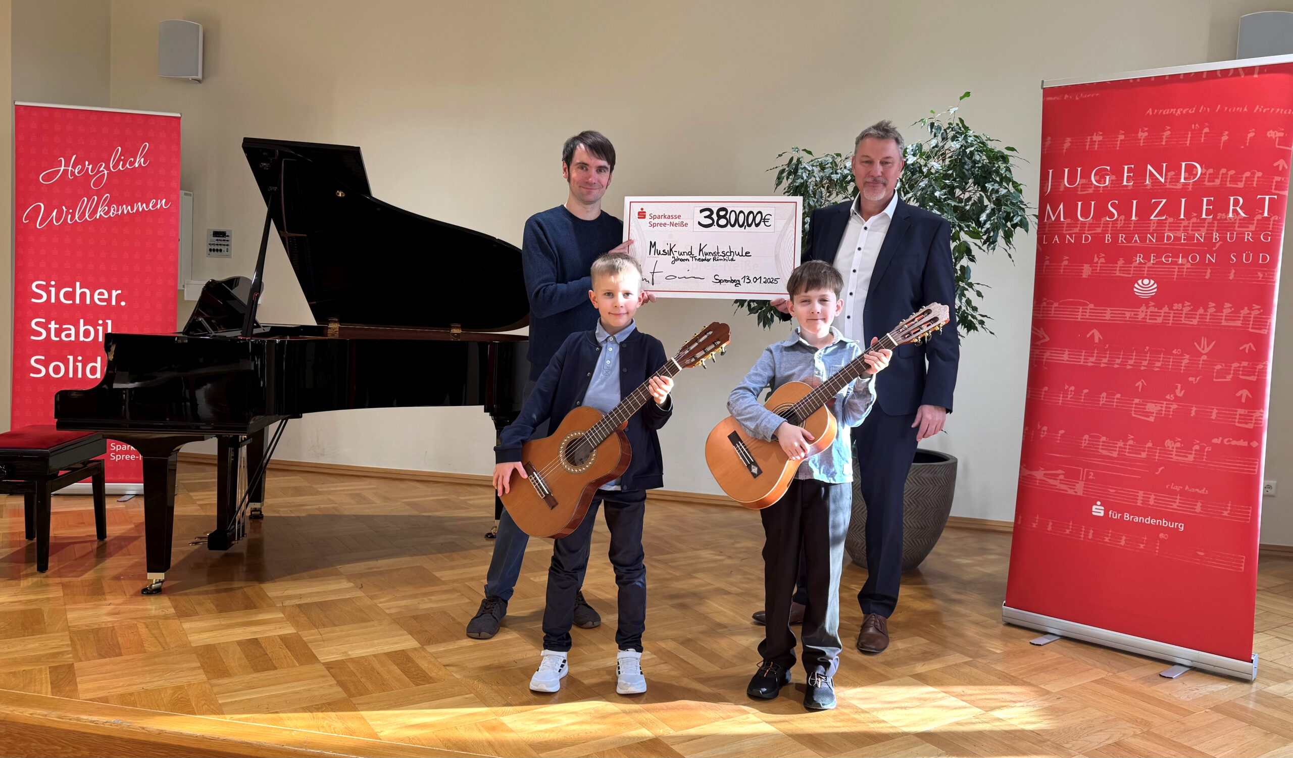 Zwei Teilnehmer von Jugend musiziert mit ihren Gitarren. Im Hintergrund wird ein Scheck von der Sparkasse Spree-Neiße überreicht.